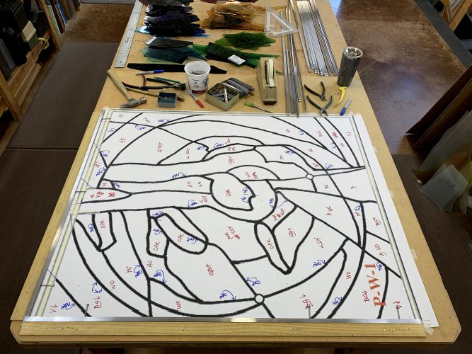 The coded cartoon for the lower panel of the West Transept Window shown taped down on the work table. Wood lath creates the corner from which pieces of glass and connecting lead calme (strips) will be added. 
