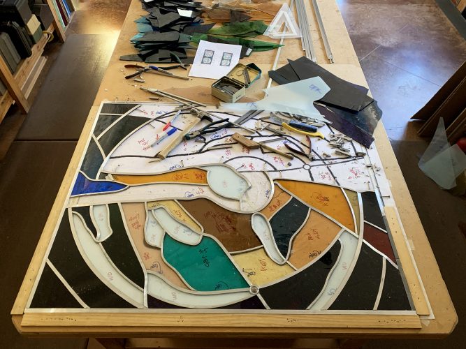BACK TO THE WORK BENCH: Glass and lead are added in a more or less diagonal direction across the cartoon. Look closely and you'll see the nails used to secure the now-unsoldered lead calme tightly against the glass. . .