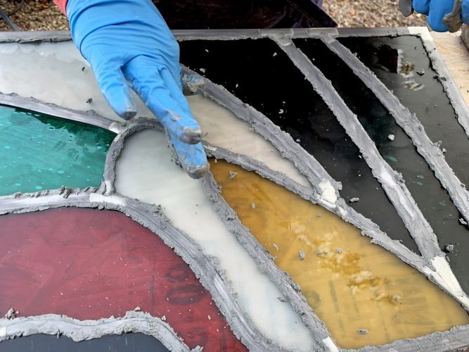 Caulking (puttying, glazing) is done by hand. Caulk is worked into the gaps between glass and lead. This not only weatherproofs the stained glass, but once the caulk has set, adds strength and rigidity to the panel. This process also darkens the lead. Once excess caulk has been removed the panel is ready for cleaning. . .